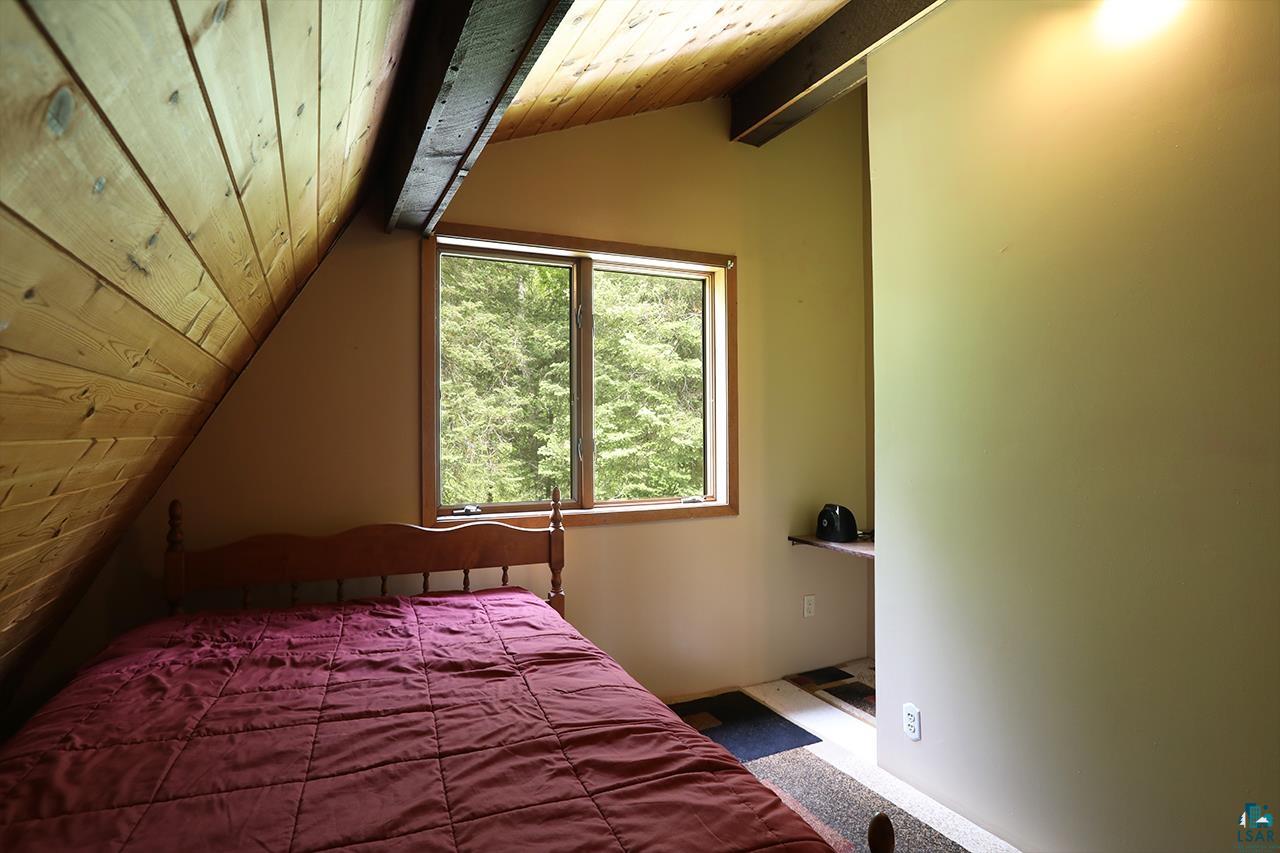 9289 Heino Road Angora, MN 55703 - Photo 19 of 37 Room featuring a prominent window, sloped wood-paneled ceiling, exposed wood beam, and light-toned walls