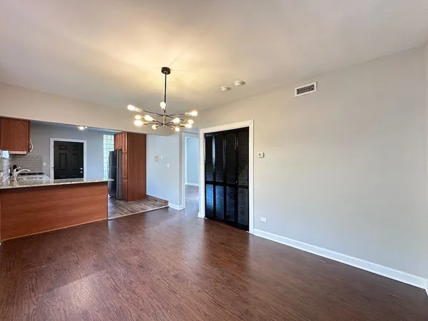 a view of an empty room with wooden floor and kitchen view