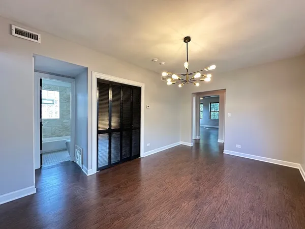 a view of an empty room with wooden floor and a kitchen