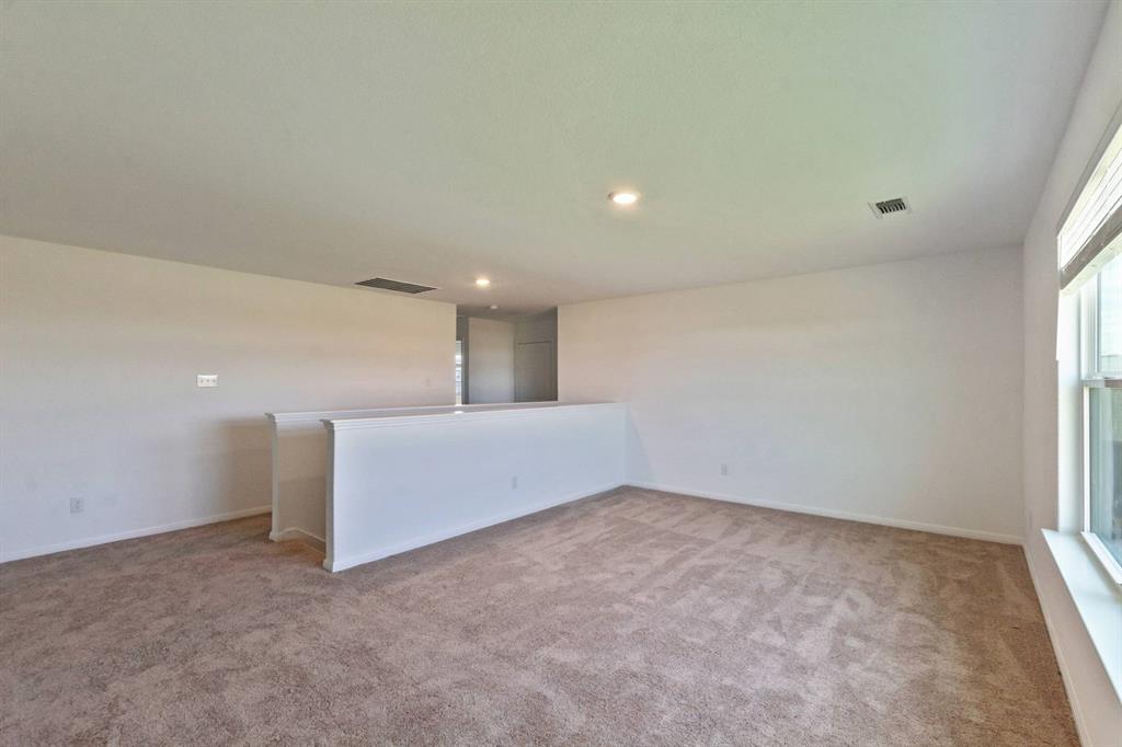 16429 Farmhouse Lane Elgin, TX 78621 - Photo 14 of 22 Versatile loft area featuring neutral-toned carpeting, ample natural light from a large window, recessed lighting, and a white half-wall railing
