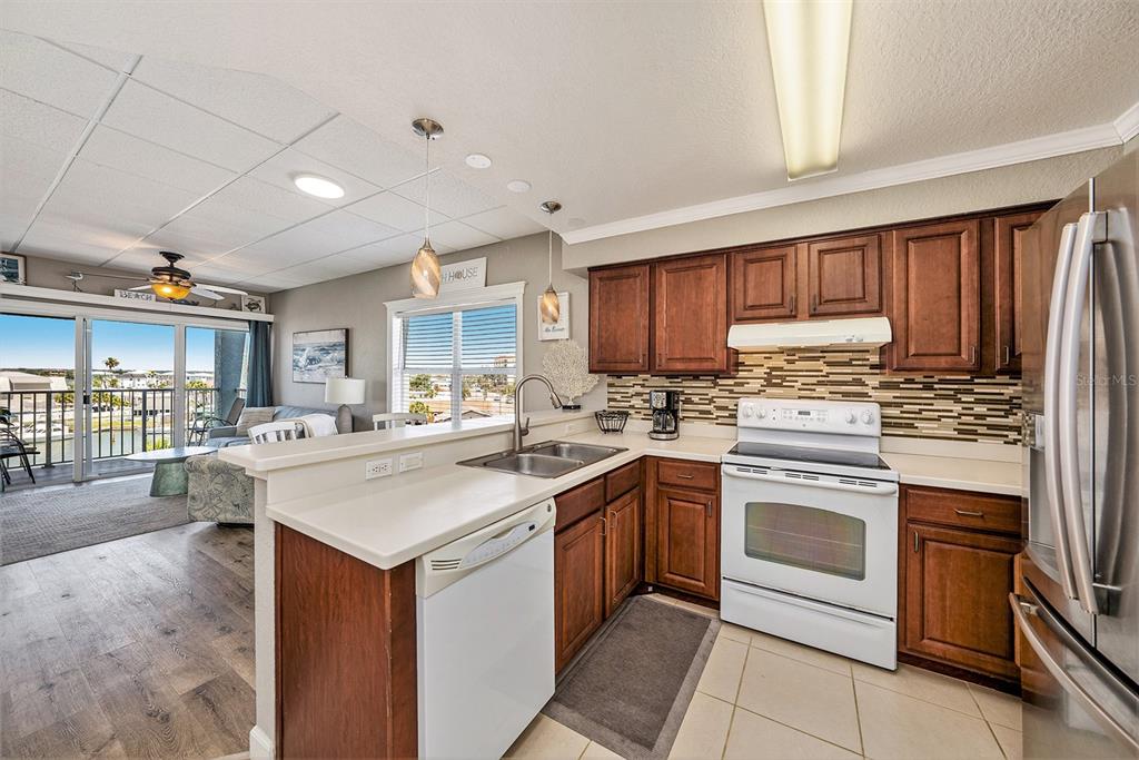 13999 Gulf Boulevard, Unit 406 St. Petersburg, FL 33708 - Photo 10 of 35 a kitchen with stainless steel appliances granite countertop a stove top oven a sink dishwasher and a refrigerator with wooden cabinets