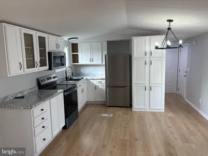 a kitchen with granite countertop a refrigerator a sink dishwasher a stove and white cabinets with wooden floor