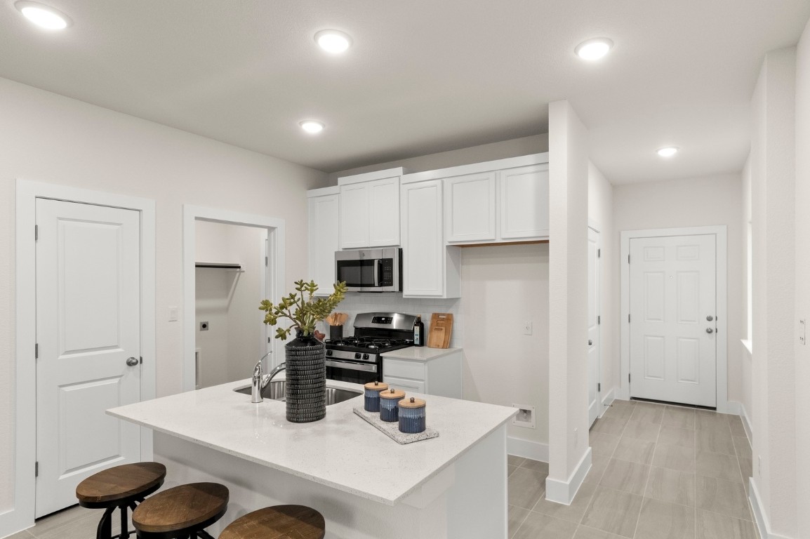701 White Steppe Way Georgetown, TX 78626 - Photo 11 of 35 Kitchen with white cabinets, a kitchen breakfast bar, stainless steel appliances, a kitchen island with sink, and light stone counters