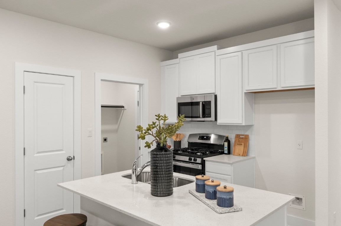 701 White Steppe Way Georgetown, TX 78626 - Photo 12 of 35 Kitchen with white cabinetry, a center island with sink, appliances with stainless steel finishes, and light stone countertops
