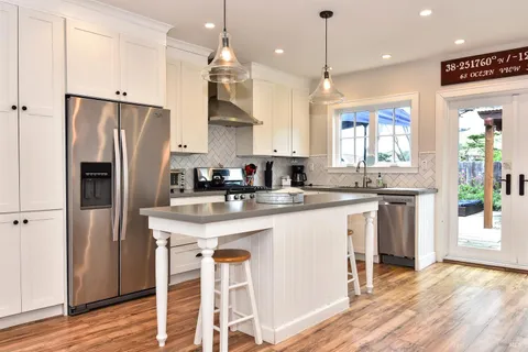 a kitchen with stainless steel appliances granite countertop a refrigerator a sink dishwasher a stove and white cabinets with wooden floor