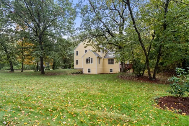 a view of a white house in front of a yard with plants and large trees