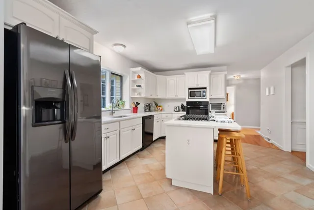 a kitchen with stainless steel appliances granite countertop a refrigerator oven a sink dishwasher and white cabinets next to a window