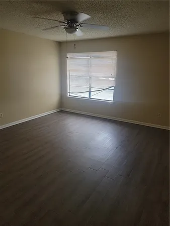 an empty room with wooden floor fan and windows