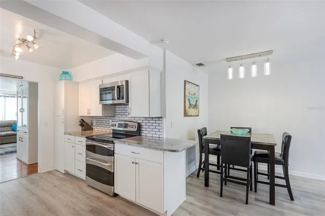 a kitchen with stainless steel appliances granite countertop a stove top oven a sink dishwasher a dining table and chairs with wooden floor