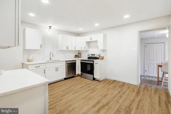 a kitchen with stainless steel appliances granite countertop a stove top oven a sink dishwasher and white cabinets with wooden floor