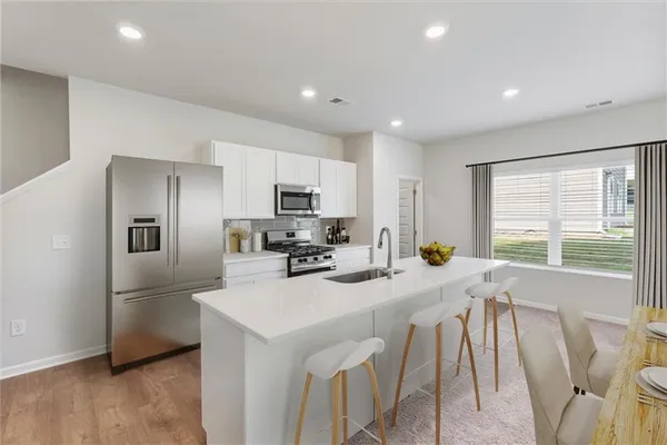 a kitchen with stainless steel appliances a refrigerator a sink a stove a microwave a dining table and chairs