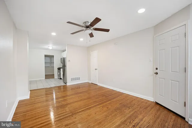 a view of an empty room with wooden floor and a ceiling fan