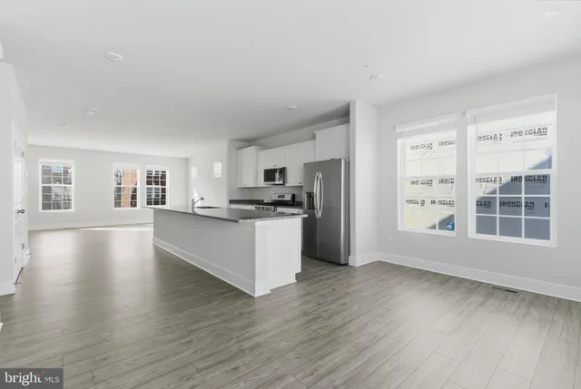 a view of an empty room with kitchen and window