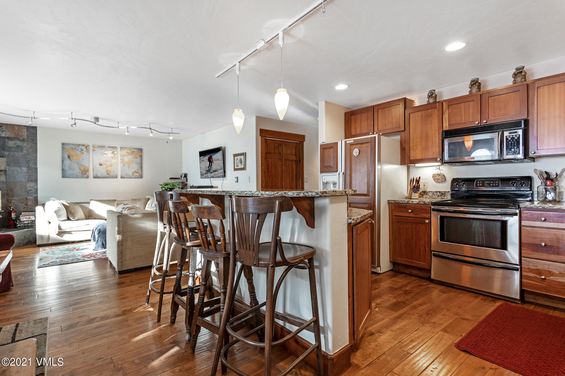 a kitchen with stainless steel appliances kitchen island granite countertop a stove a refrigerator a dining table and chairs with wooden floor