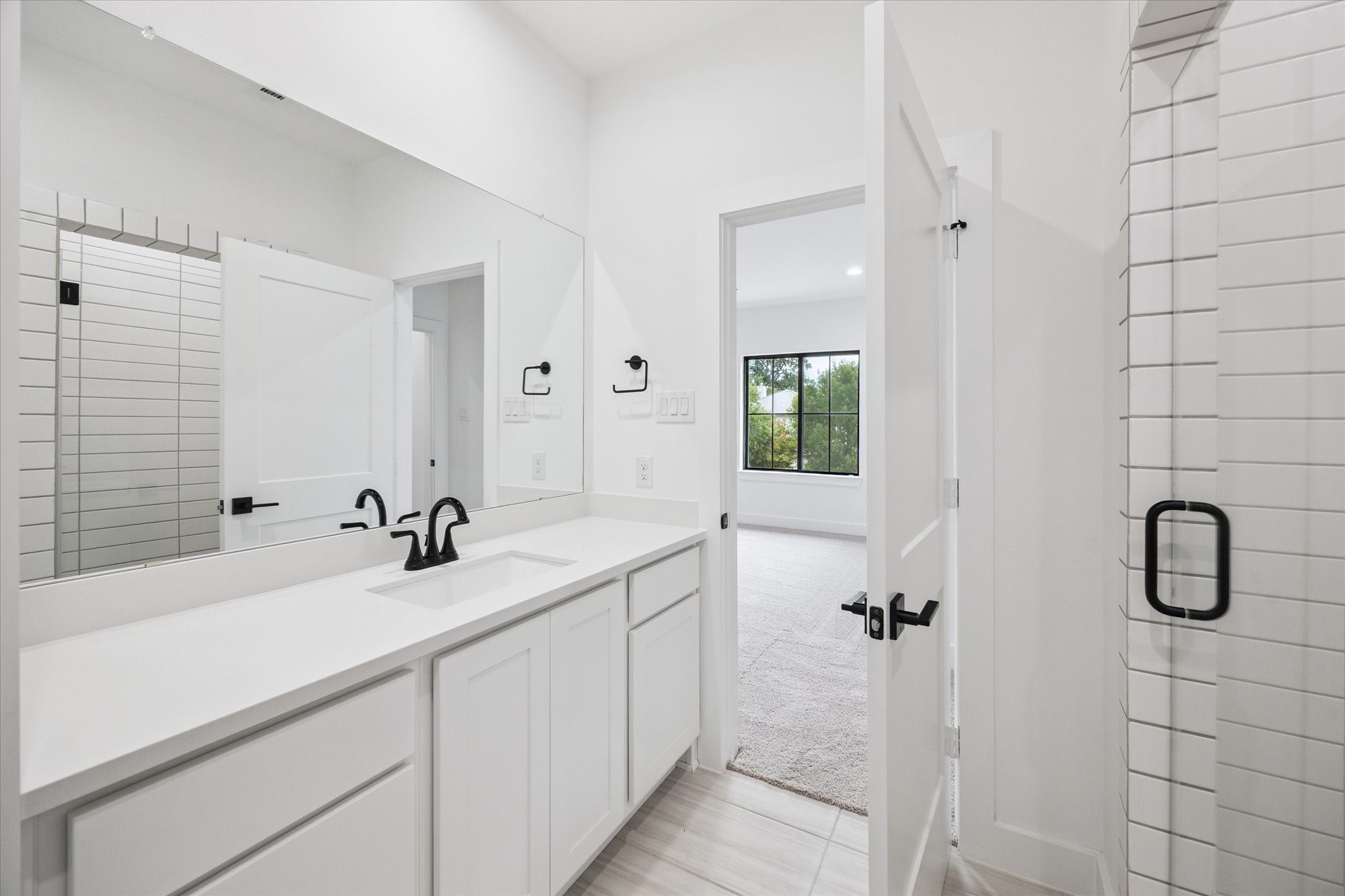1201 Confederate Road Houston, TX 77055 - Photo 20 of 33 Bright and tailored, this ensuite bathroom features a glass-enclosed shower with vertical tile detail, sleek matte black fixtures, and clean white finishes throughout. Direct access to the adjoining bedroom enhances privacy and ease.