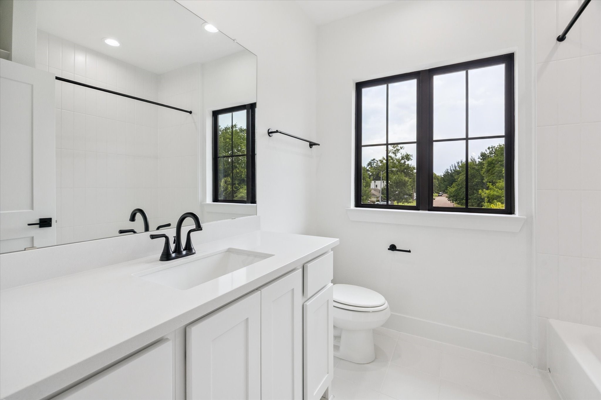 1201 Confederate Road Houston, TX 77055 - Photo 22 of 33 Crisp and bright, this secondary bathroom features clean white finishes, black matte fixtures, and natural light pouring in through a large window. Subtle contrast and simple detailing create a polished, timeless look.