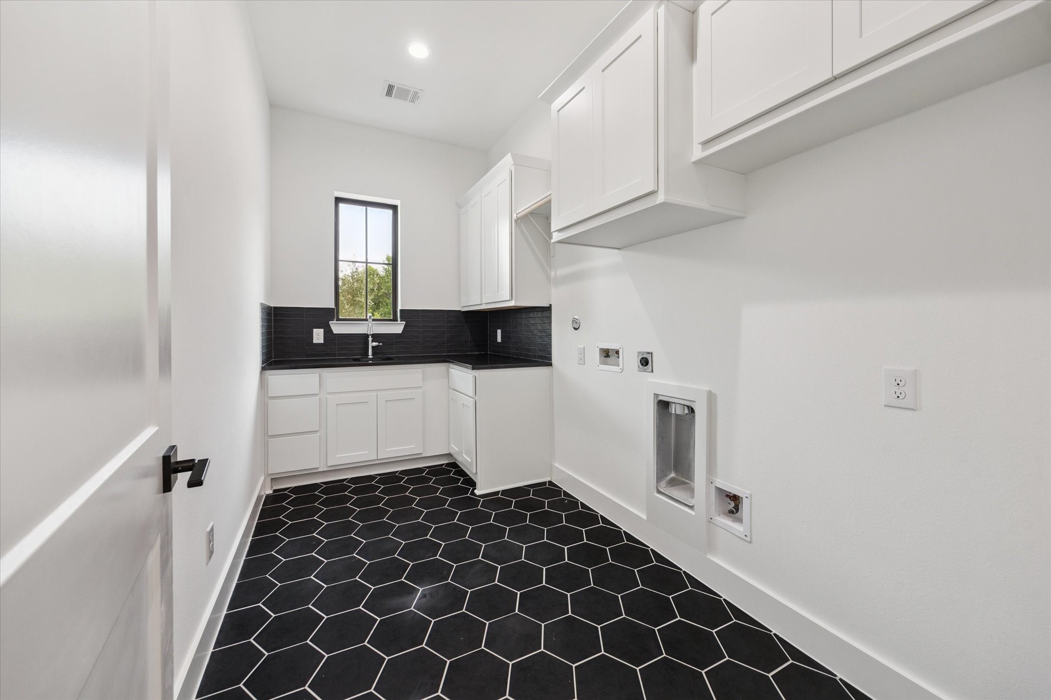 1201 Confederate Road Houston, TX 77055 - Photo 24 of 33 The utility room features bold black hex tile flooring, abundant cabinetry, a deep sink, and hanging space—blending practicality with sleek, modern design. A large window fills the space with natural light, making everyday tasks feel elevated.