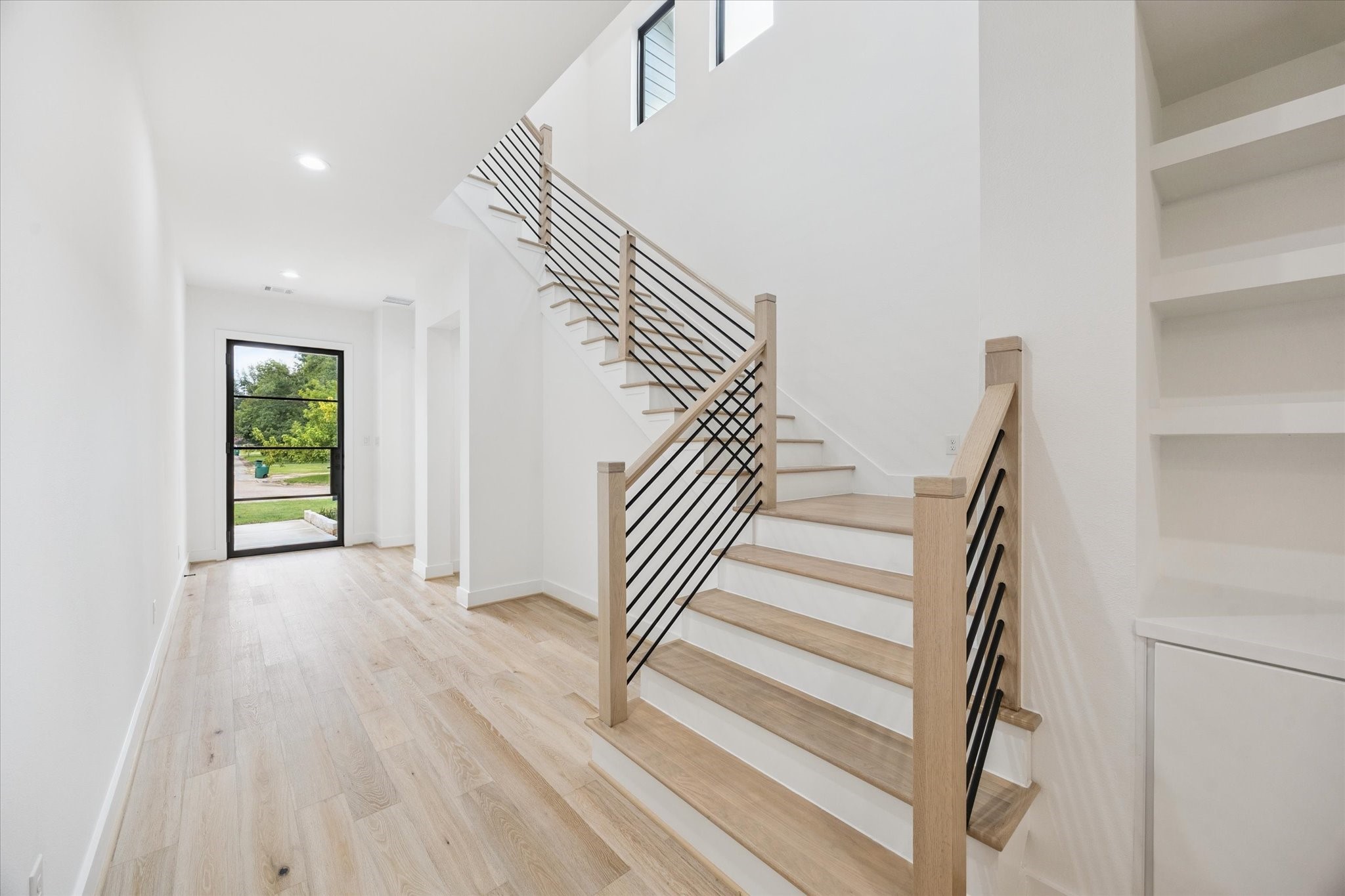 1201 Confederate Road Houston, TX 77055 - Photo 3 of 33 A striking staircase with light oak treads and sleek black metal balusters anchors the foyer, blending modern edge with warm tones. Oversized windows and open shelving add both light and function to this thoughtfully designed transition space.