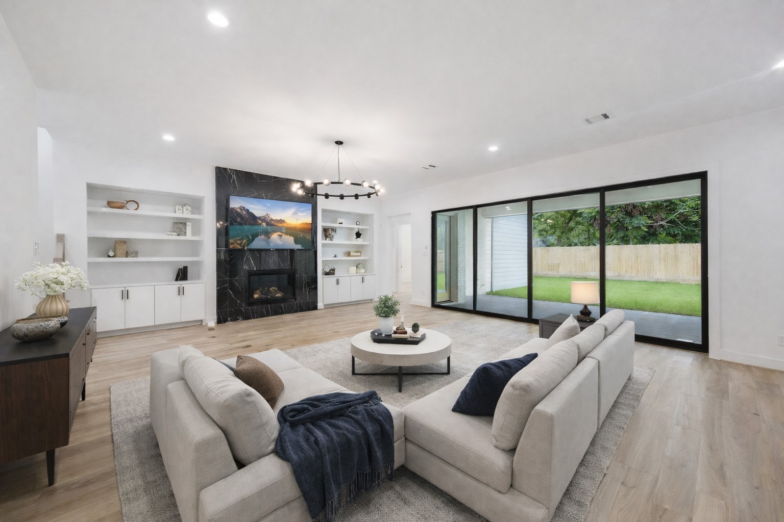 1201 Confederate Road Houston, TX 77055 - Photo 5 of 33 Expansive and bright, the living room features a dramatic black marble fireplace flanked by custom built-ins, wide-plank floors, and a statement light fixture. A full wall of sliding glass doors opens to the covered patio, creating a seamless indoor-outdoor connection perfect for entertaining. *Virtually Staged*