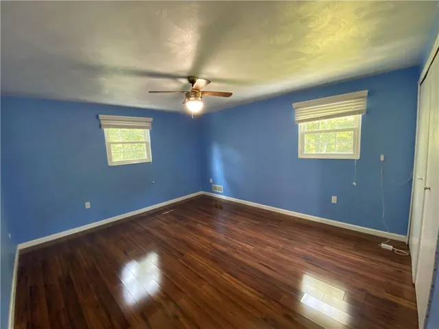 an empty room with wooden floor fan and windows