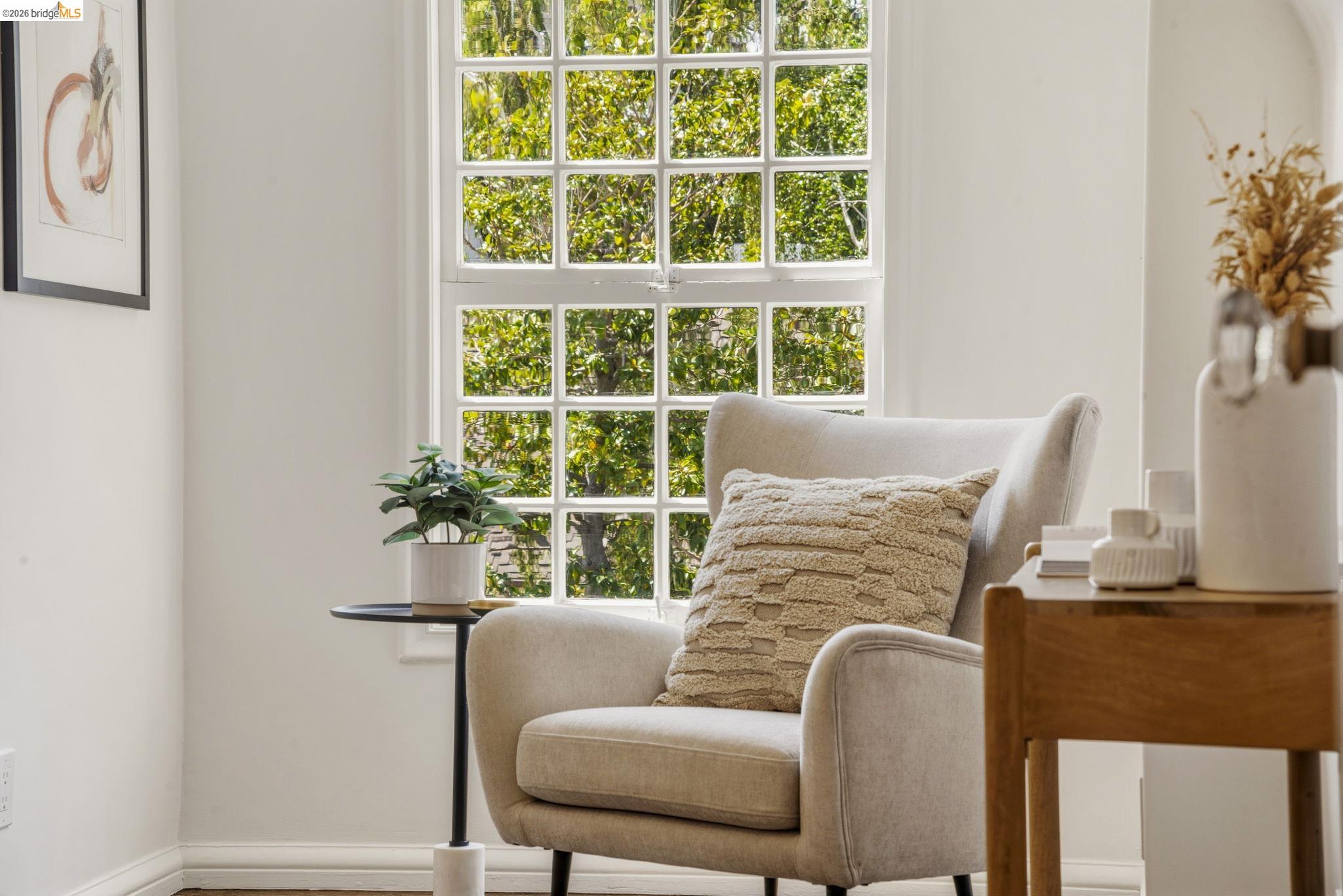 1087 Hubert Road Oakland, CA 94610 - Photo 22 of 67 White paneled window with green tree foliage outside, set against a light-colored wall with white baseboards and wood-finish flooring