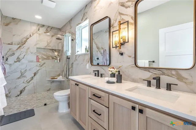 a bathroom with a double vanity sink toilet mirror and shower