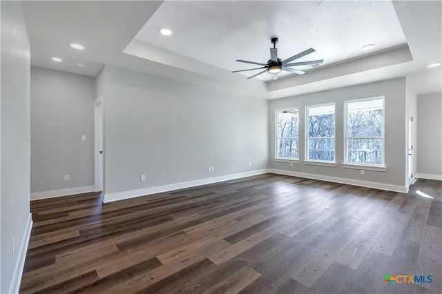 an empty room with wooden floor chandelier fan and windows