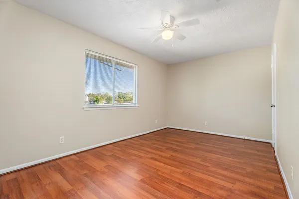 an empty room with wooden floor chandelier fan and windows