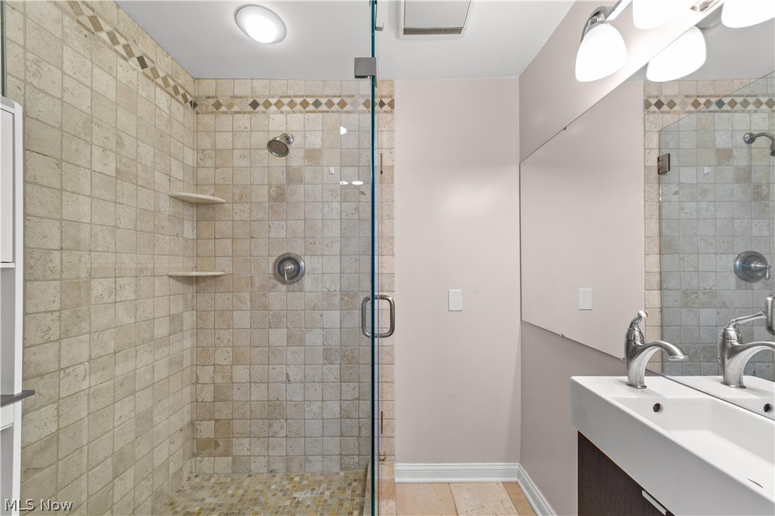 3806 Westwood Road University Heights, OH 44118 - Photo 19 of 41 Glass-enclosed shower featuring natural stone tile walls with decorative border, built-in shelving, and a pebble floor