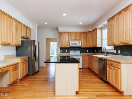 a large kitchen with stainless steel appliances granite countertop a stove a sink a refrigerator and white cabinets with wooden floor