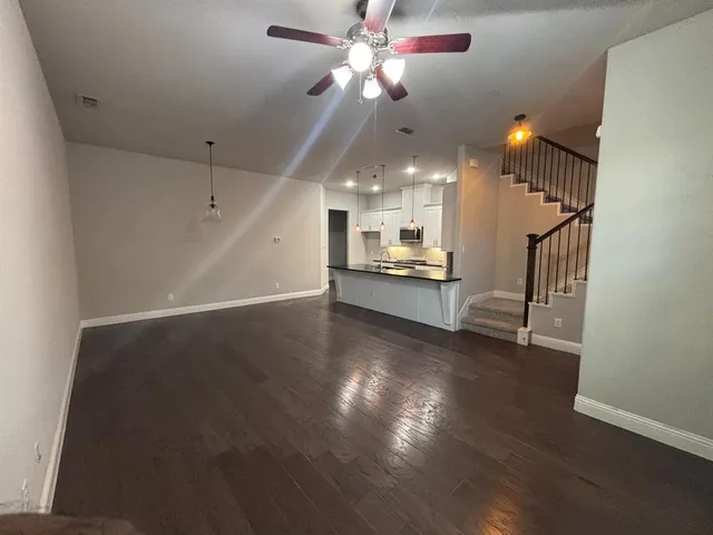 a view of a room with wooden floor a ceiling fan and kitchen view
