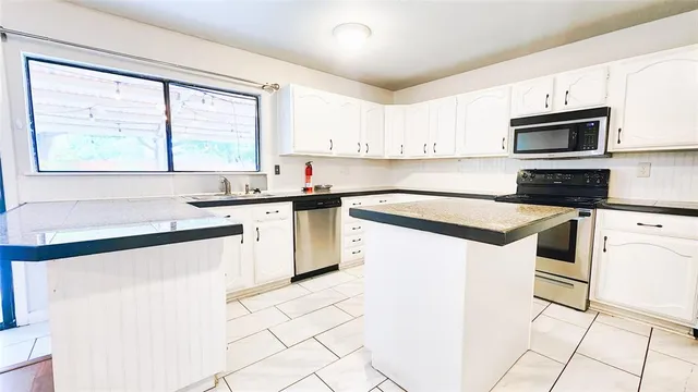 a kitchen with granite countertop white cabinets white appliances a sink and a window