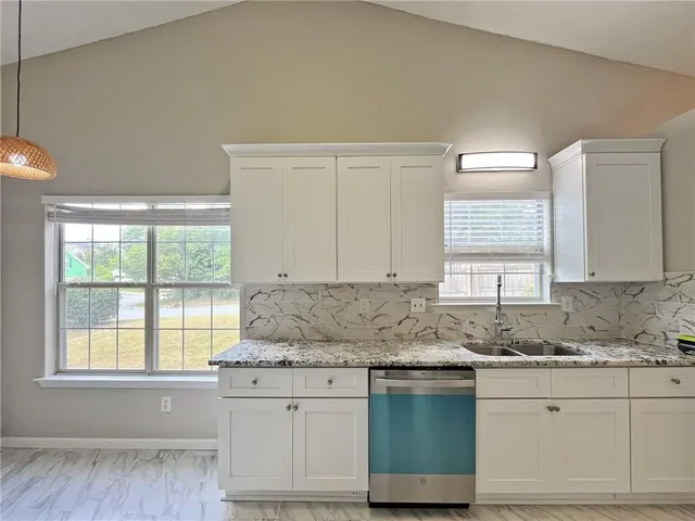 a kitchen with granite countertop white cabinets white appliances a sink and a large window