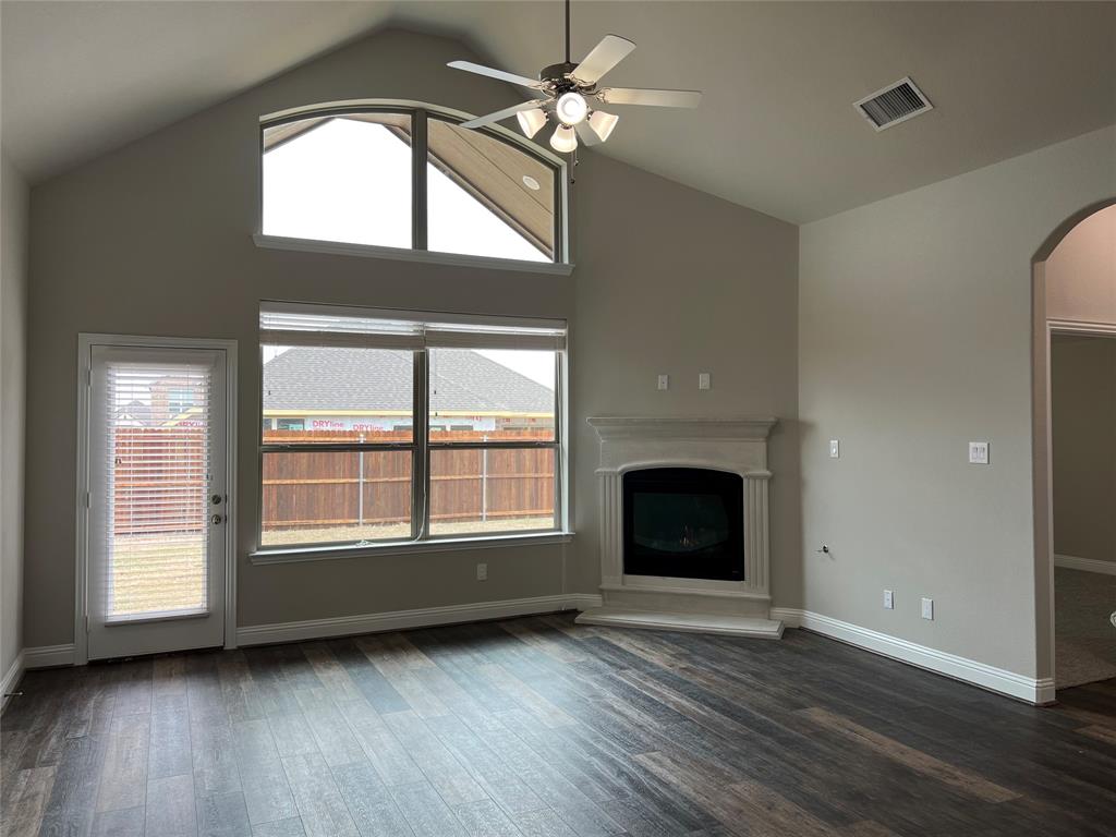 277 Eagle Ridge Forney, TX 75126 - Photo 5 of 19 Unfurnished living room featuring a ceiling fan, arched walkways, a fireplace with raised hearth, dark wood-style floors, and high vaulted ceiling