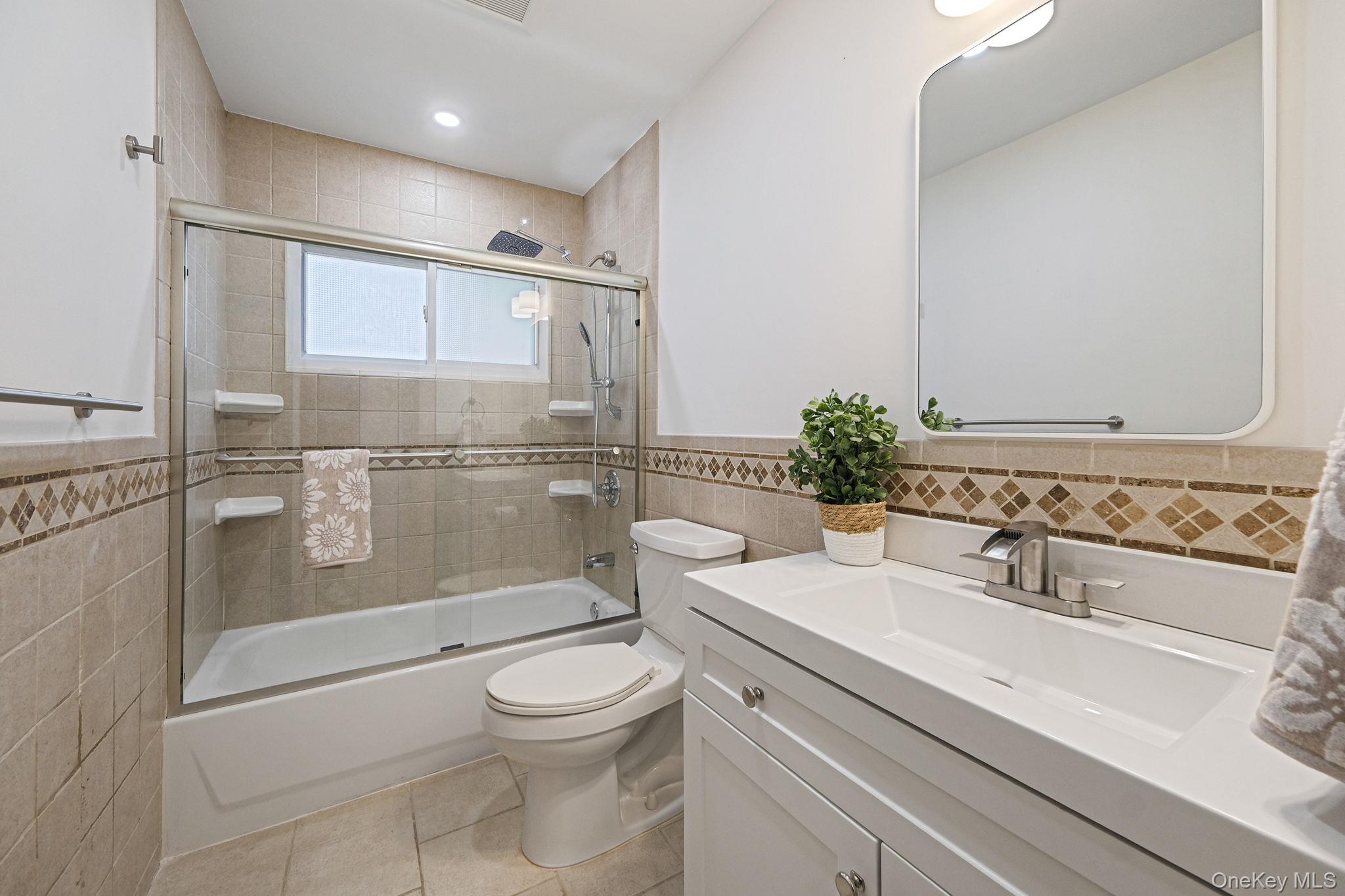 11 Wildwood Road Ridge, NY 11961 - Photo 15 of 17 Full bath featuring tile walls, shower / bath combination with glass door, vanity, light tile patterned floors, and wainscoting