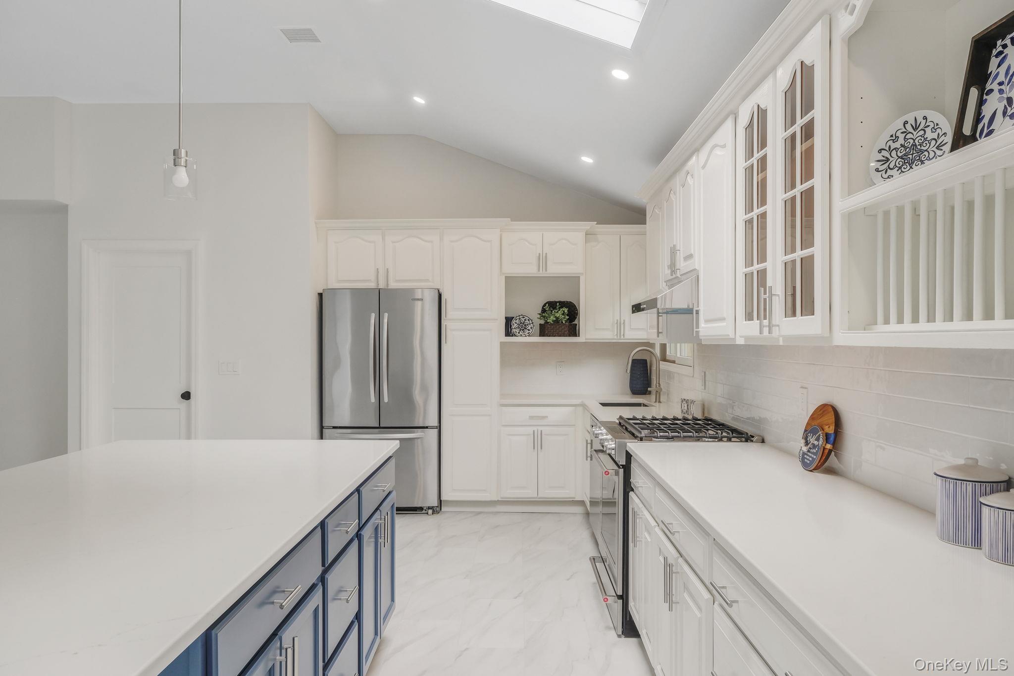 11 Wildwood Road Ridge, NY 11961 - Photo 5 of 17 Kitchen with blue cabinetry, white cabinetry, appliances with stainless steel finishes, glass insert cabinets, and vaulted ceiling