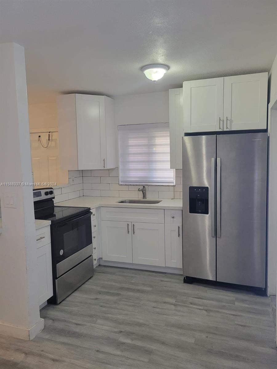 5922 Pierce Street, Unit 1 Hollywood, FL 33021 - Photo 3 of 7 a kitchen with a white stove refrigerator and white cabinets with wooden floor