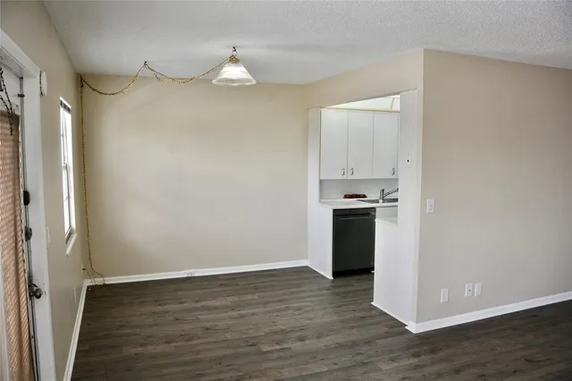 a view of an empty room with wooden floor and a kitchen