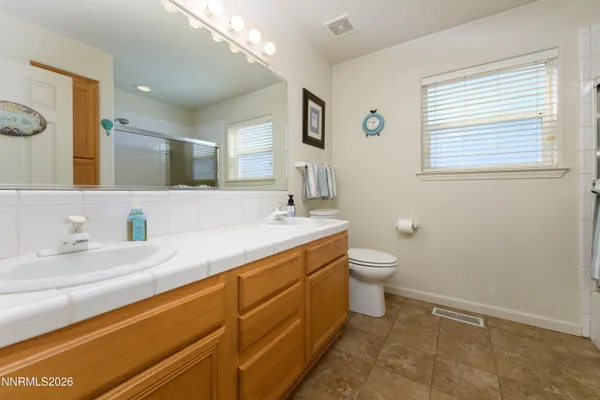 a bathroom with a granite countertop toilet a sink a mirror and a window