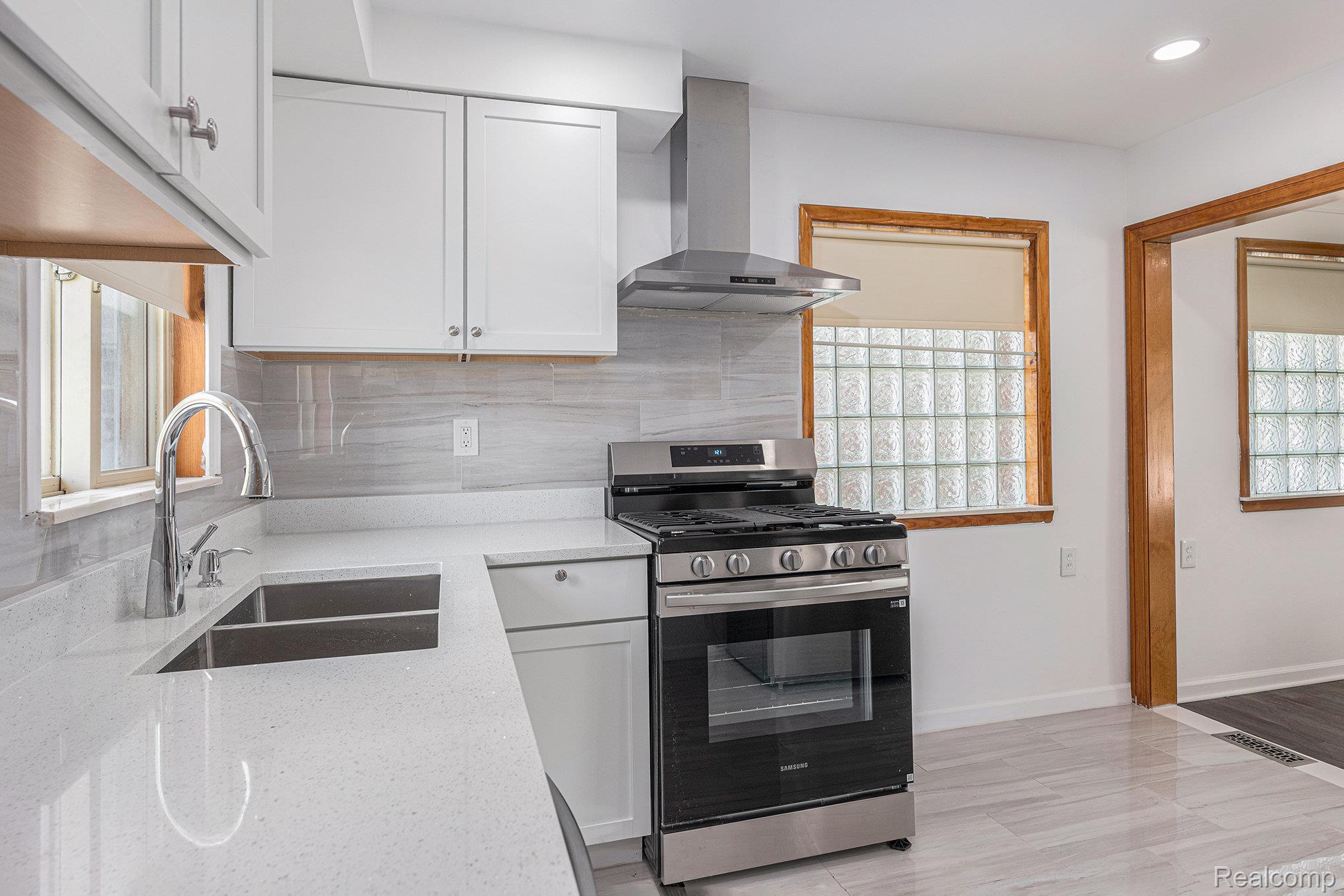 5239 East Thirteen Mile Road Warren, MI 48092 - Photo 7 of 16 Modern kitchen featuring white shaker cabinetry, stainless steel appliances, a chrome gooseneck faucet, light-toned countertops, and a full-height tile backsplash