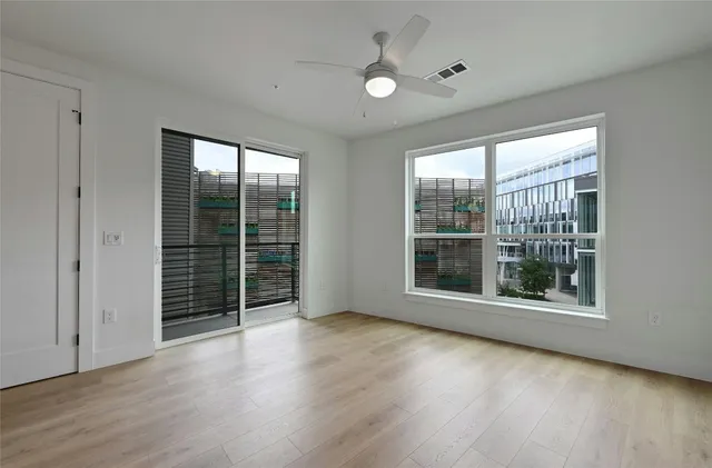 a view of an empty room with wooden floor and fan with window