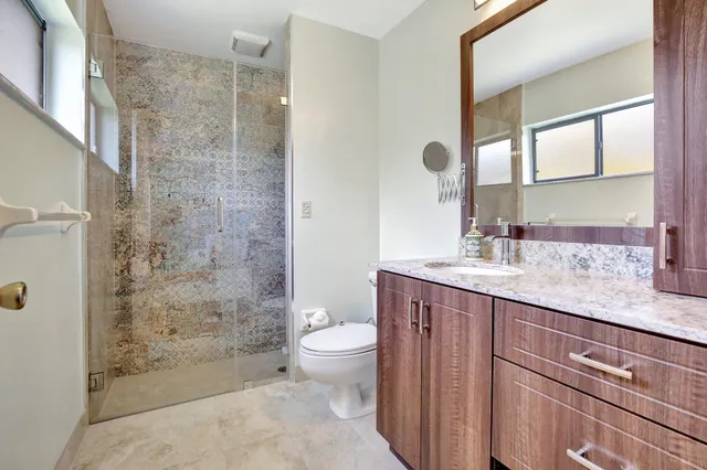 a bathroom with a granite countertop sink a toilet a mirror and shower