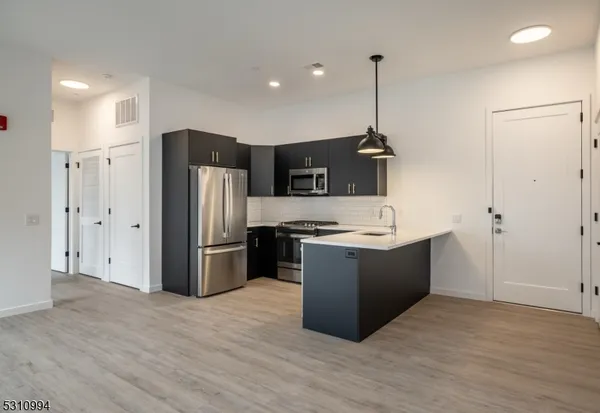 a kitchen with stainless steel appliances granite countertop a refrigerator a sink dishwasher a oven and a wooden floor