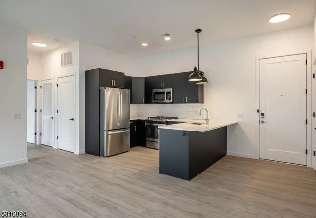 a kitchen with stainless steel appliances granite countertop a refrigerator a sink dishwasher a oven and a wooden floor