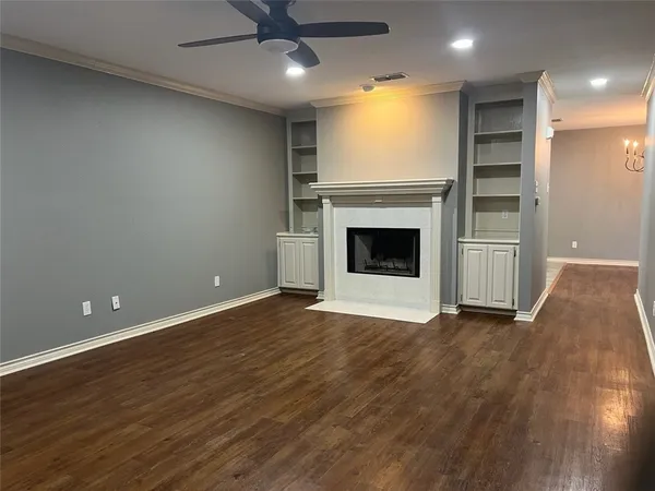 an empty room with wooden floor a ceiling fan a fireplace and windows