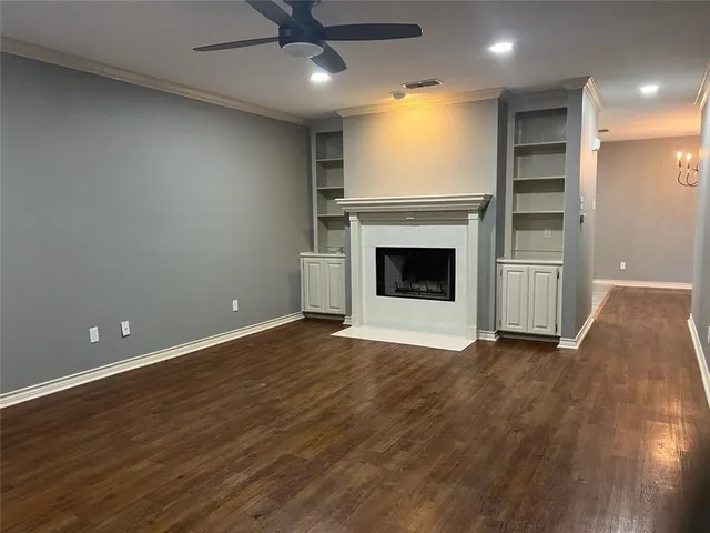 an empty room with wooden floor a ceiling fan a fireplace and windows