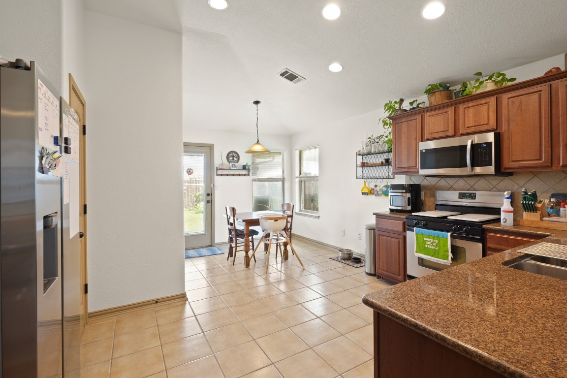 11012 Short Springs Drive Austin, TX 78754 - Photo 11 of 28 a kitchen with stainless steel appliances granite countertop a refrigerator a stove a sink a dining table and chairs with the view of living room