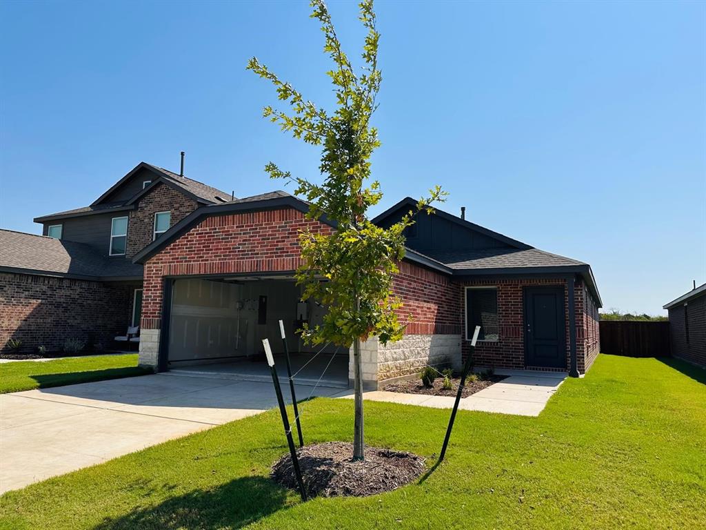 View of front of home featuring a front yard, an attached garage, driveway, brick siding, and board and batten siding