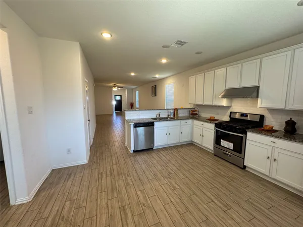 a kitchen with stainless steel appliances granite countertop a stove top oven a sink dishwasher and a refrigerator with wooden floor