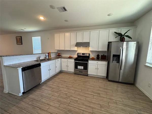 a kitchen with granite countertop a refrigerator a sink dishwasher and white cabinets with wooden floor